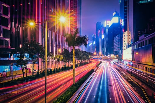 Street traffic in Hong Kong at night. Office skyscraper buildings and busy traffic on highway road with blurred cars light trails. Hong Kong, China