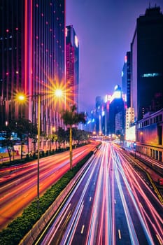 Street traffic in Hong Kong at night. Office skyscraper buildings and busy traffic on highway road with blurred cars light trails. Hong Kong, China