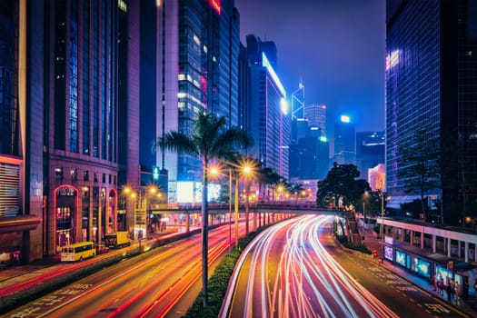 Street traffic in Hong Kong at night. Office skyscraper buildings and busy traffic on highway road with blurred cars light trails. Hong Kong, China