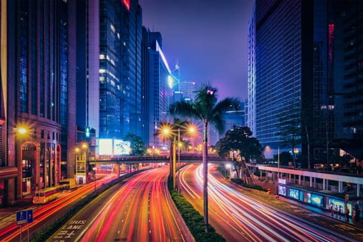 Street traffic in Hong Kong at night. Office skyscraper buildings and busy traffic on highway road with blurred cars light trails. Hong Kong, China