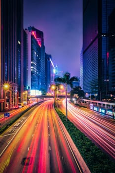 Street traffic in Hong Kong at night. Office skyscraper buildings and busy traffic on highway road with blurred cars light trails. Hong Kong, China