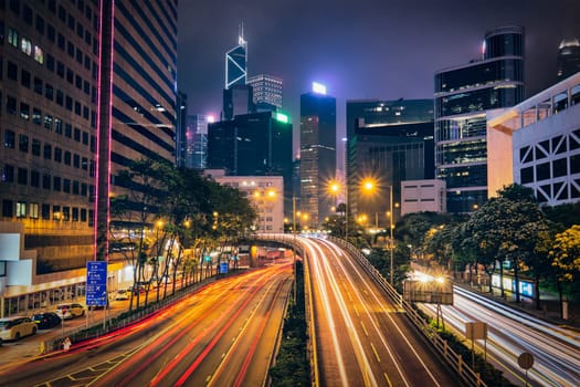 Street traffic in Hong Kong at night. Office skyscraper buildings and busy traffic on highway road with blurred cars light trails. Hong Kong, China