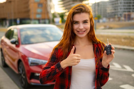 Young smiling woman holding in hand car keys sand shows thumb up like gesture standing in the street.