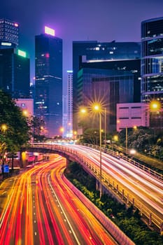 Street traffic in Hong Kong at night. Office skyscraper buildings and busy traffic on highway road with blurred cars light trails. Hong Kong, China