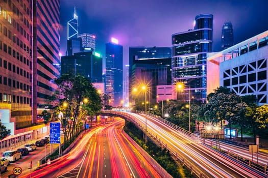 Street traffic in Hong Kong at night. Office skyscraper buildings and busy traffic on highway road with blurred cars light trails. Hong Kong, China