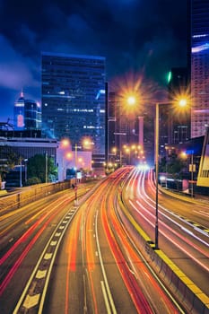 Street traffic in Hong Kong at night. Office skyscraper buildings and busy traffic on highway road with blurred cars light trails. Hong Kong, China