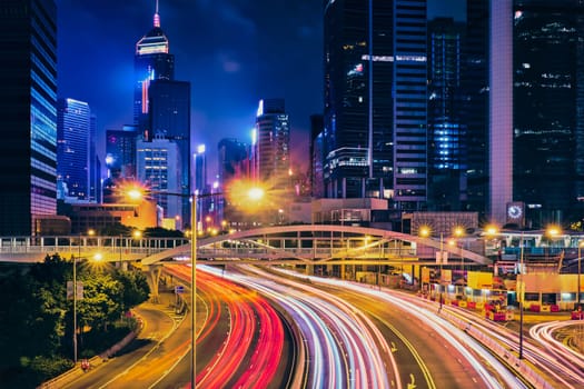 Street traffic in Hong Kong at night. Office skyscraper buildings and busy traffic on highway road with blurred cars light trails. Hong Kong, China