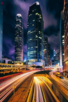 Street traffic in Hong Kong at night. Office skyscraper buildings and busy traffic on highway road with blurred cars light trails. Hong Kong, China