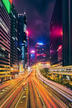 Street traffic in Hong Kong at night. Office skyscraper buildings and busy traffic on highway road with blurred cars light trails. Hong Kong, China