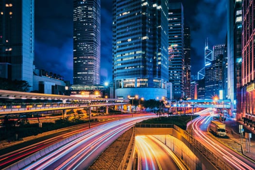 Street traffic in Hong Kong at night. Office skyscraper buildings and busy traffic on highway road with blurred cars light trails. Hong Kong, China