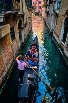 VENICE, ITALY - JUNE 27, 2018: Narrow canal between colorful old houses with gondola boat with tourists and gonolier in Venice, Italy