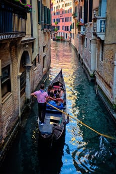 VENICE, ITALY - JUNE 27, 2018: Narrow canal between colorful old houses with gondola boat with tourists and gonolier in Venice, Italy