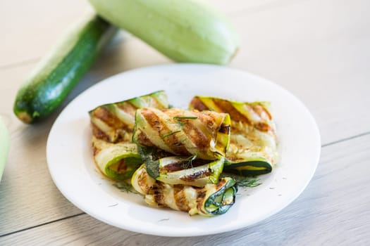 Grilled zucchini pieces with garlic sauce in a white plate. Light gray wooden background.