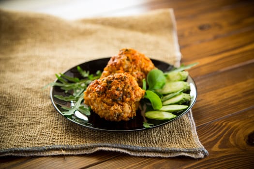 Cooked meatballs in a plate with fresh vegetables, on a wooden table.