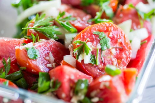 Spicy snack tomatoes with garlic, herbs, seasonings and onions in a glass bowl on a wooden table.