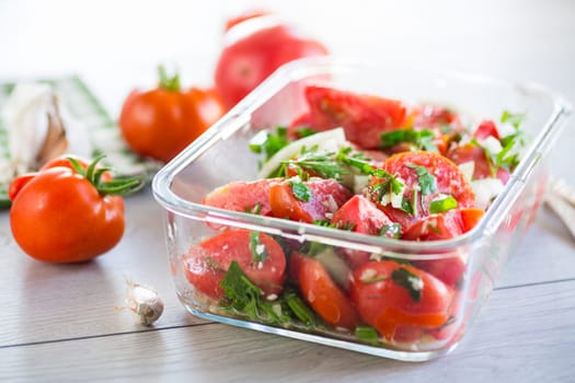 Spicy snack tomatoes with garlic, herbs, seasonings and onions in a glass bowl on a wooden table.