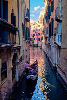 VENICE, ITALY - JUNE 27, 2018: Narrow canal between colorful old houses with gondola boat with tourists and gonolier in Venice, Italy