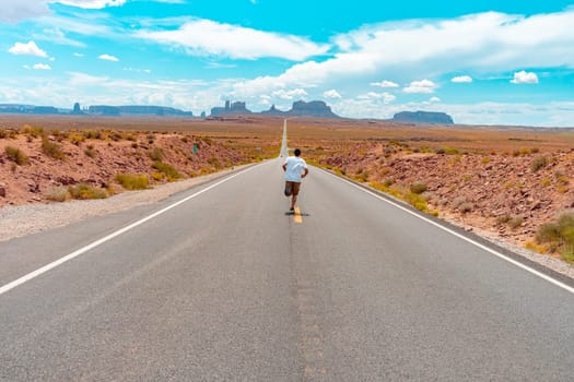 Attractive young man from back view sitting in the middle of American straight road in the desert. High quality photo