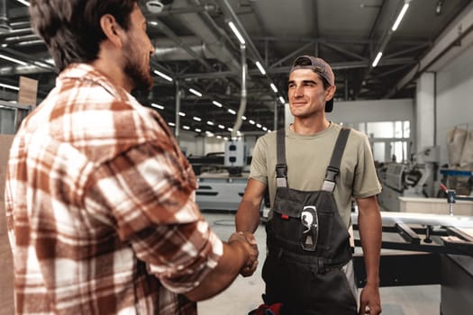Two men shaking hands on background of workshop close up