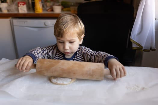 Family cooking - a little boy works with a rolling pin with raw dough. Mid shot
