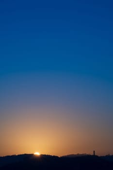 Stunning image of a yellow sun rising behind mountains, with a blue sky turning orange at dawn.