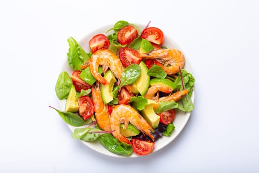 Healthy salad with grilled shrimps, avocado, cherry tomatoes and green leaves on white plate isolated on white background top view. Clean eating, nutrition and dieting concept..