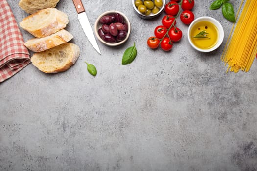 Food composition with sliced ciabatta, olives, olive oil, spaghetti, fresh basil, cherry tomatoes on gray concrete stone rustic background top view, copy space. Italian cuisine concept