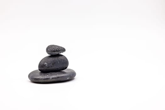 A cairn consisting of three black stones in front of white background in studio