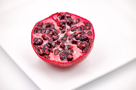 Close-up of a pomegranate half on a plate cropped in front of white background as studio shot