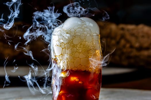 Whisky Smoke. Smoking whiskey with ice and orange on a dark background. Cognac with smoking branch of lavender. Experimental alcoholic cocktail in a glass with smoking rosemary.
