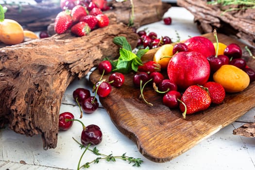 Fresh berries and fruits on a old-fashioned wooden plate on rotten stump. Countryside. Outdoor