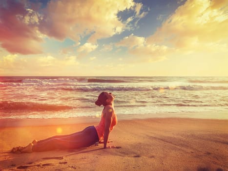 Yoga outdoors on beach - woman practices Ashtanga Vinyasa yoga Surya Namaskar Sun Salutation asana Urdhva Mukha Svanasana - upward facing dog pose on sunset. With light leak and lens flare