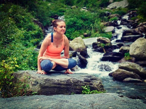 Yoga exercise outdoors - woman doing Ashtanga Vinyasa Yoga arm balance strength training asana Tolasana - scales pose at waterfall in Himalayas. Vintage retro effect filtered hipster style image