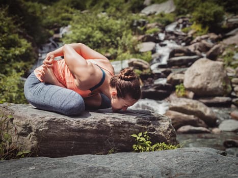 Vintage retro effect filtered hipster style image of Young sporty fit woman doing yoga - meditating in Baddha Padmasana (Bound Lotus Pose) outdoors at tropical waterfall