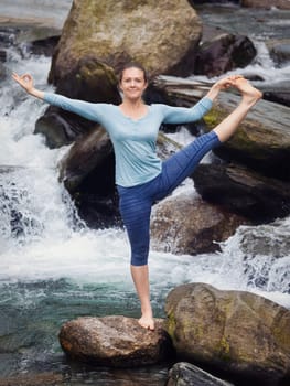 Yoga outdoors - woman doing Ashtanga Vinyasa Yoga balance asana Utthita Hasta Padangushthasana Extended Hand-To-Big-Toe Pose position outdoors at waterfall. Vintage retro effect filtered hipster style