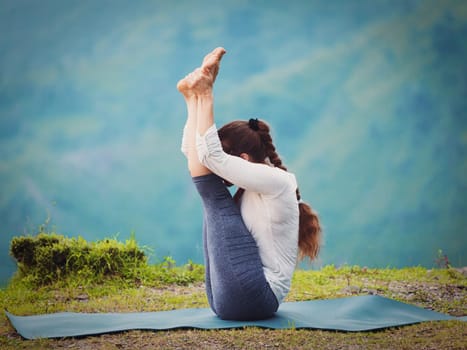 Yoga - sporty fit woman practices Ashtanga Vinyasa yoga asana Urdhva mukha paschimottanasana - upward facing intense west stretch oudoors. Vintage retro effect filtered hipster style image.