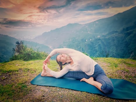 Yoga outdoors - young sporty fit woman doing Hatha Yoga asana janu sirsasana - Revolved Head-to-Knee Pose - in. Vintage retro effect filtered hipster style image.