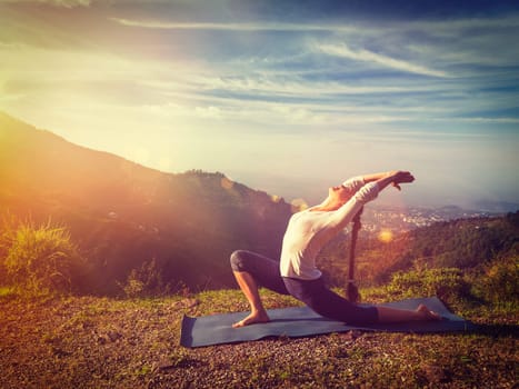Yoga outdoors - sporty fit woman practices yoga Anjaneyasana low crescent lunge pose outdoors in mountains in morning. With light leak and lens flare. Vintage retro effect filtered hipster style image