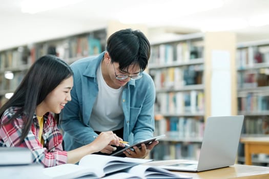 Young students campus helps friend catching up and learning. University students in cooperation with their assignment at library. Group of young people sitting at table reading books. Education and learning concept.