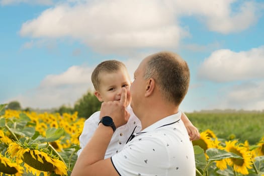 Father's day concept. Family. A little boy in his father's arms, laughing and playing happily against the blue sky in a field with yellow sunflowers. A symbol of peace. Symbol of Ukraine. Close-up. copy space.