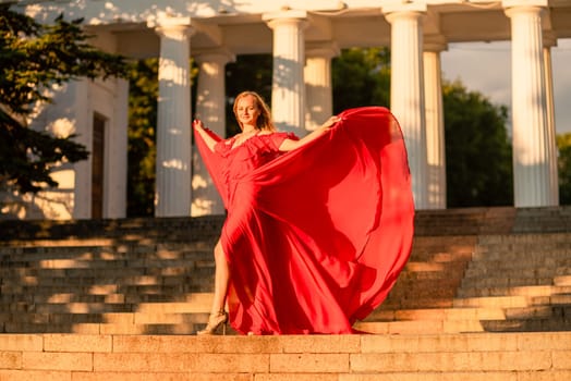 A woman in a long red dress against the backdrop of sunrise, bright golden light of the sun's rays. The concept of femininity, harmony