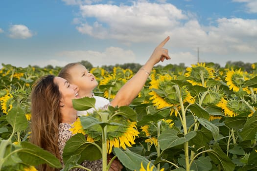 Family concept. A little boy in his mother's arms, gently hugging. Stand in a field with yellow sunflowers on a summer background. blue sky Peace symbol. Symbol of Ukraine.