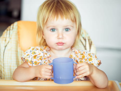 beautiful little girl sitting in a highchair and drinks