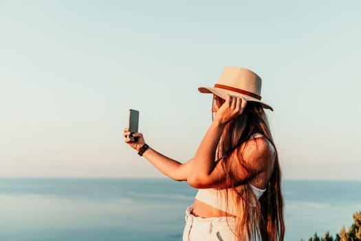 Selfie woman in hat, white tank top and shorts makes selfie shot mobile phone post photo social network outdoors on sea background beach people vacation lifestyle travel concept