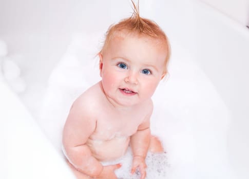 pretty smiling baby girl is taking a bath with a foam