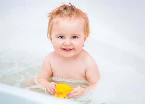 happy 1 year-old girl bathes in a bath with a duck
