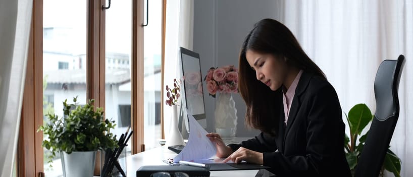 Serious female accountant comparing corporate income for previous year with current one at her workstation.