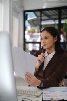 Professional businesswoman analyzing sales statistics document, using laptop at her working desk.