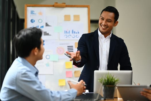 Smiling millennial male leader asking question, interacting with team at corporate meeting.