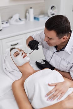 male beautician applies the mask to the face of beautiful woman in the spa salon. facial skin care concept.